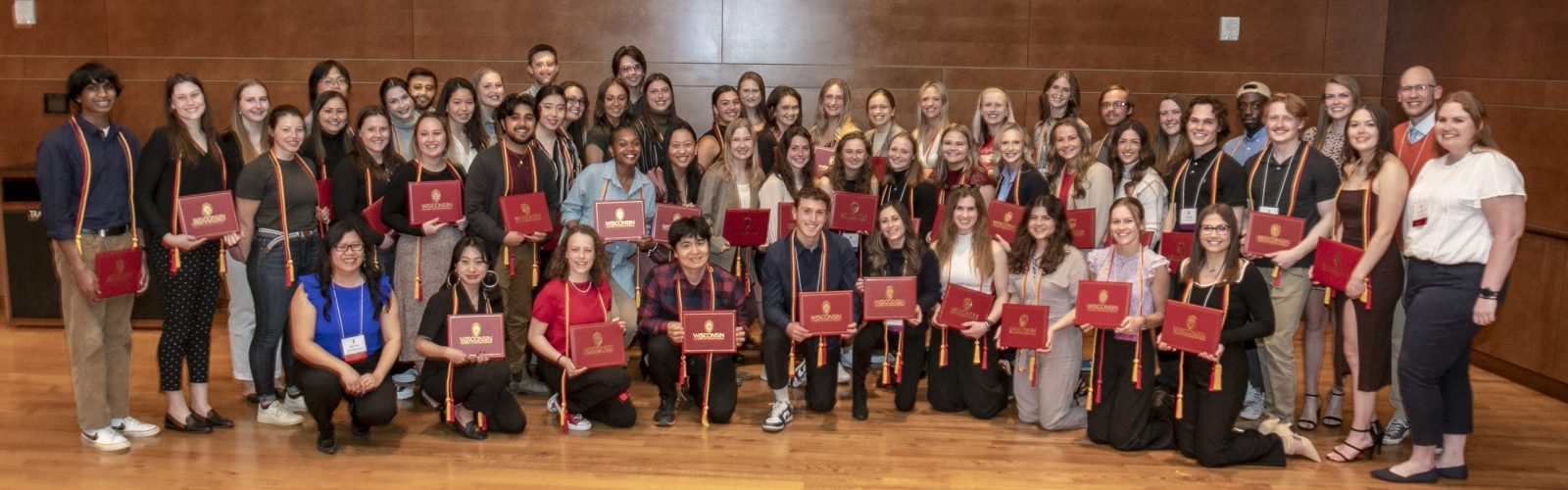 A picture taken on May 2nd, 2023 of the recipients of the University of Wisconsin Leadership Certificate as well as staff from the Center for Leadership and Involvement. There are three rows of people and approximately 65 students included in the photo. Students are wearing the red and gold graduation cords and holding the certificates that they receive at the recognition ceremony. The picture was taken by photographer Brian Ebner.