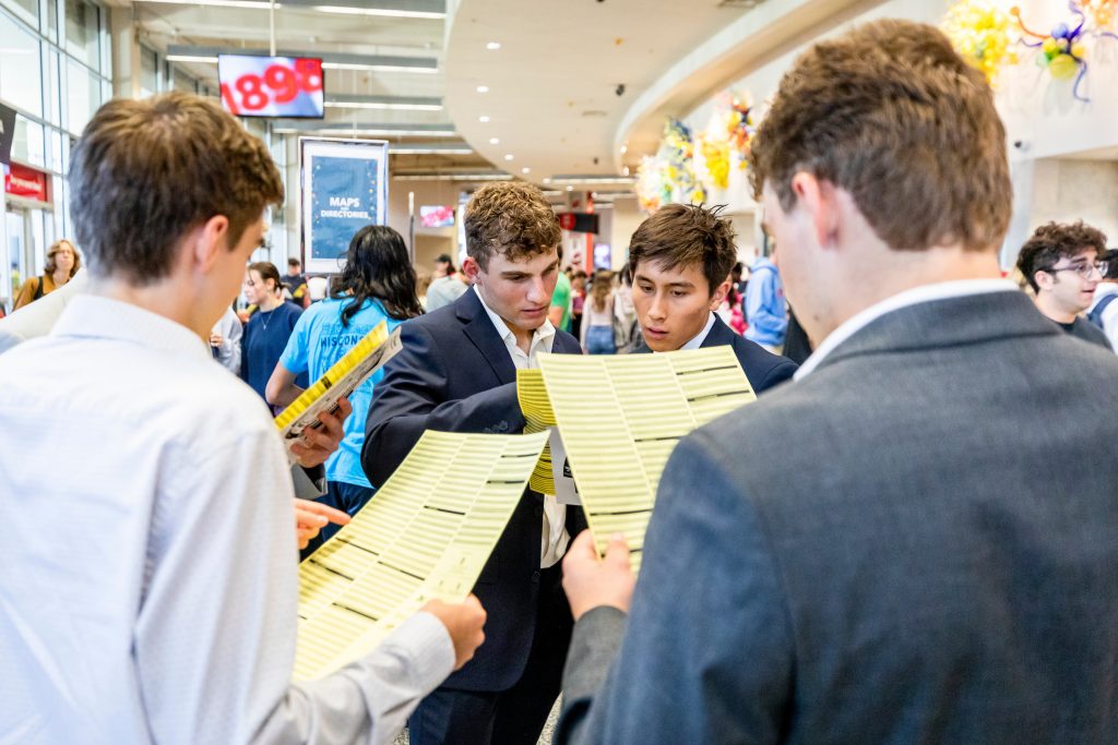 A group of students plan out their route while looking through maps of student organizations present during the Fall Student Organization Fair at the Kohl Center