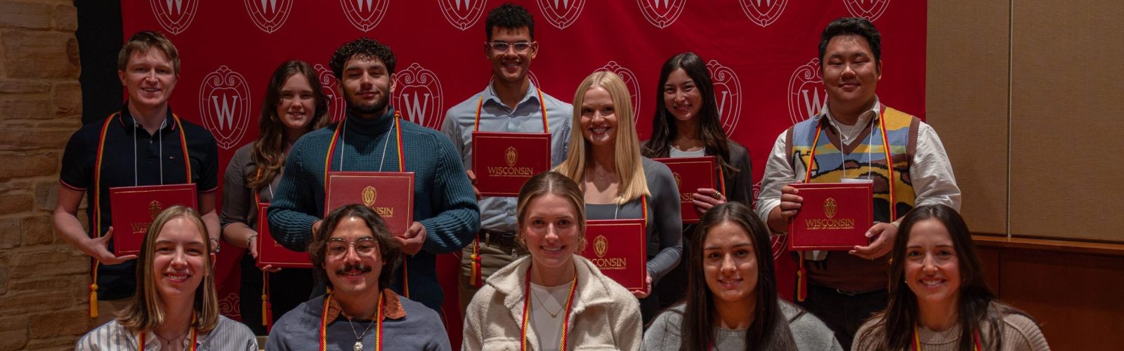 A picture taken on December 2, 2024 of the recipients of the University of Wisconsin Leadership Certificate. There are approximately 12 students wearing red and gold graduation cords and holding the certificates that they receive at the recognition ceremony.