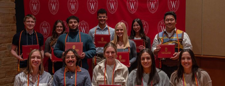 A picture taken on December 2, 2024 of the recipients of the University of Wisconsin Leadership Certificate. There are approximately 12 students wearing red and gold graduation cords and holding the certificates that they receive at the recognition ceremony.