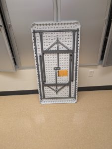 A four foot table, not set up, leaning against the wall to showcase what it looks like not set up.