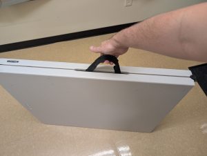 A foldable 6-foot table all folded up with a hand holding the handle to show how it can be carried.