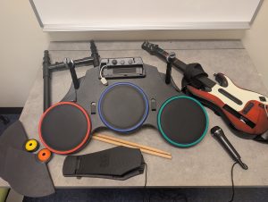 Wii Guitar Hero instruments including drums with cymbals, sticks, and pedal, guitar, and microphone.