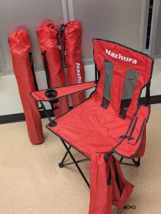 Four, red foldable chairs. Three are all folded and in their bags. One is unfolded to show what it looks like.
