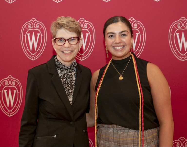 Two women standing in front of a UW Madison logo background