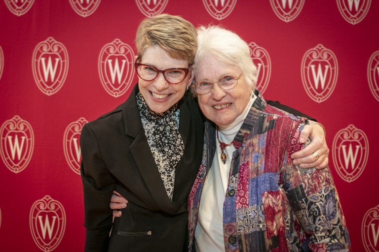 Two women hugging each other in front of the UW Madison logo