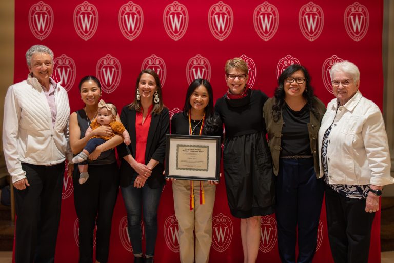Seven women and 1 baby in front of the UW Madison logo