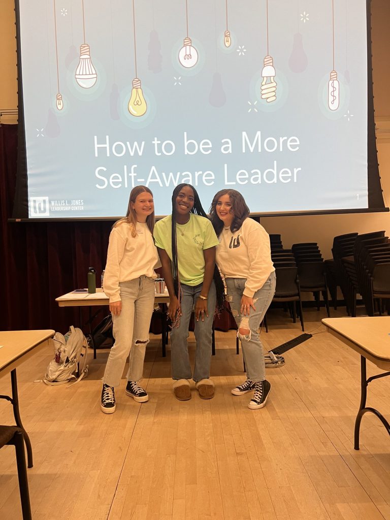 three students stand in front of a presentation slide that reads