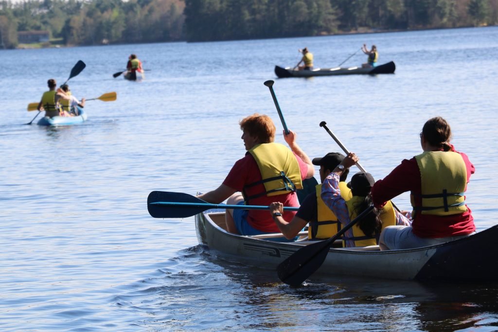 3 students wearing yellow life jackets canoe.