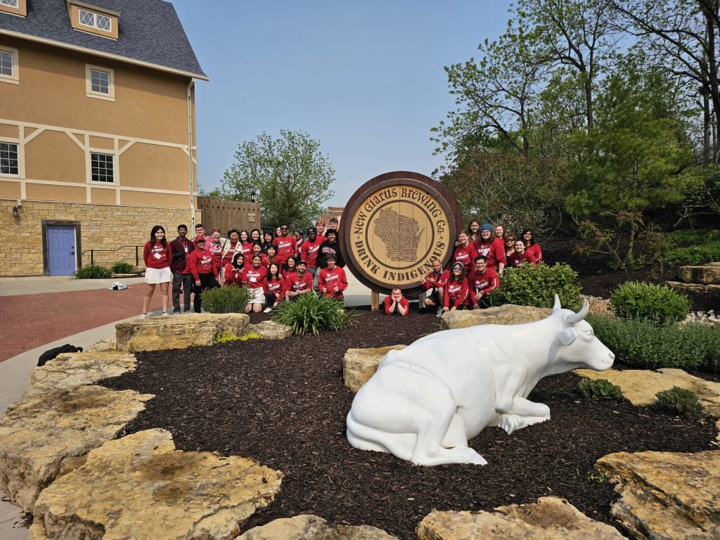 A group of 35 students wear dark red, long-sleeve shirts that say 