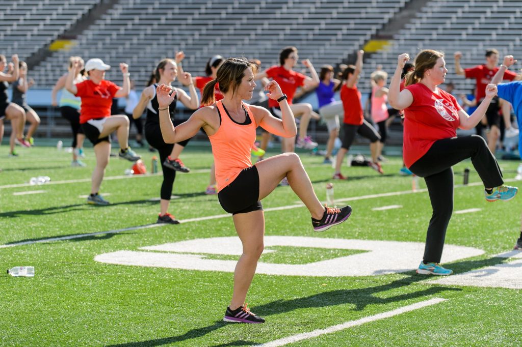 A group of people working out at the field doing different cardio exercises.
