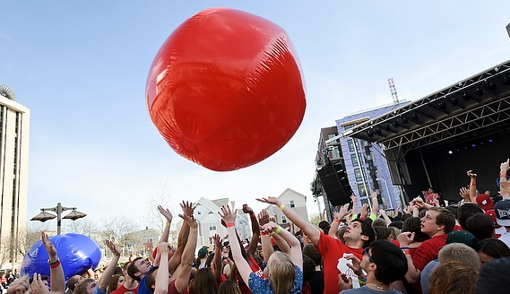 Students at music festival throwing a large red ball over crowd.