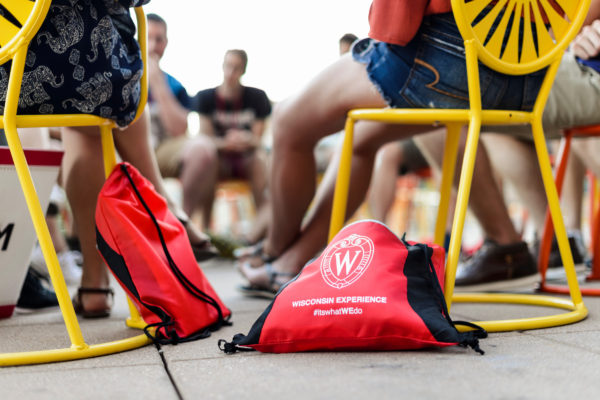 Two red UW-Madison drawstring leaning against yellow chairs with people sitting in the background.