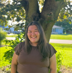 A woman smiles while standing in front of a tree.