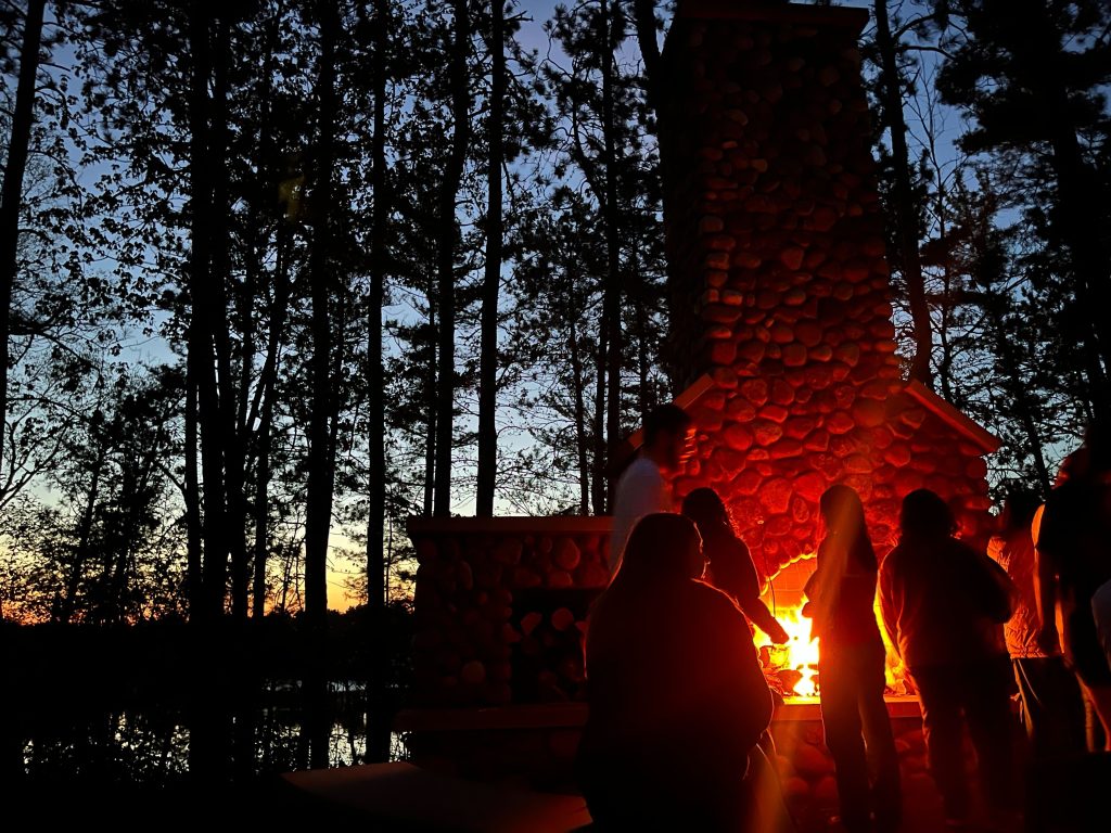 An outdoor evening shot of WEBT students gathered around a brick campfire at the Central Wisconsin Environmental Station.