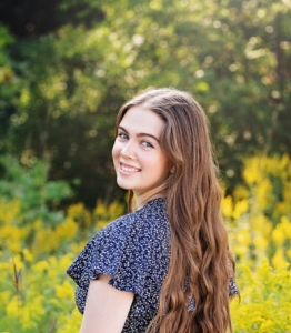 A woman smiling with flowers behind her.