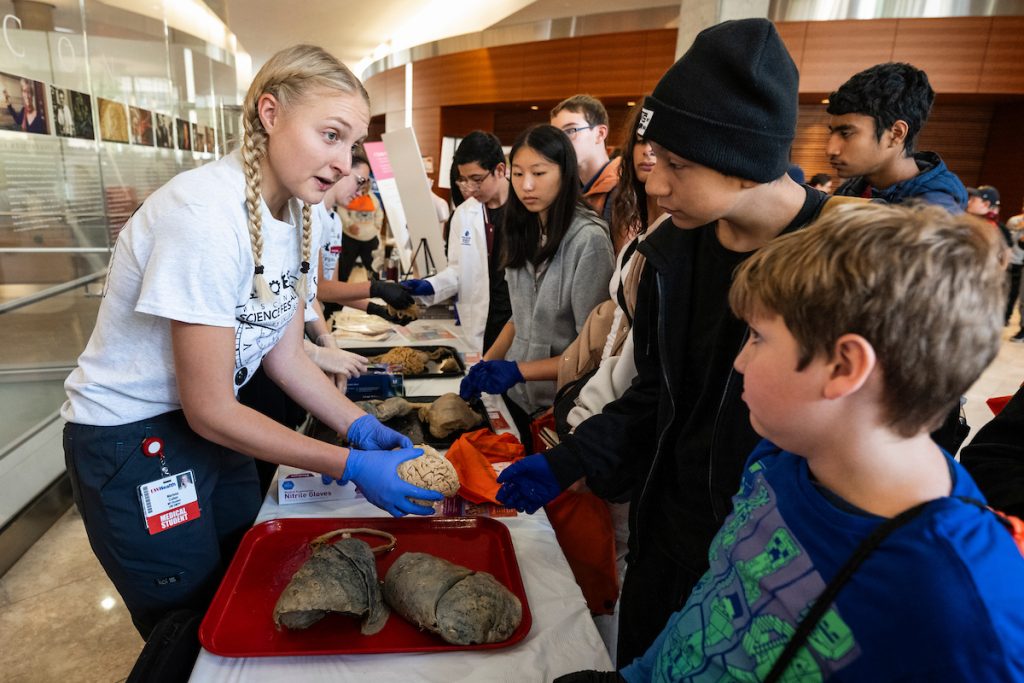 a college student holds an organ in front of an elementary student